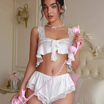 A woman wearing a white satin ruffle sleepwear set with lace-trimmed crop top and ruffle sleeves, holding a pink phone, in a room with a vintage aesthetic.